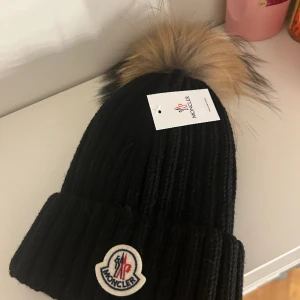 moncler mössa - Mössan är inte äkta, aldrig använd, äkta päls på mössan som går att ta bort sitter med knapp, Onesize
