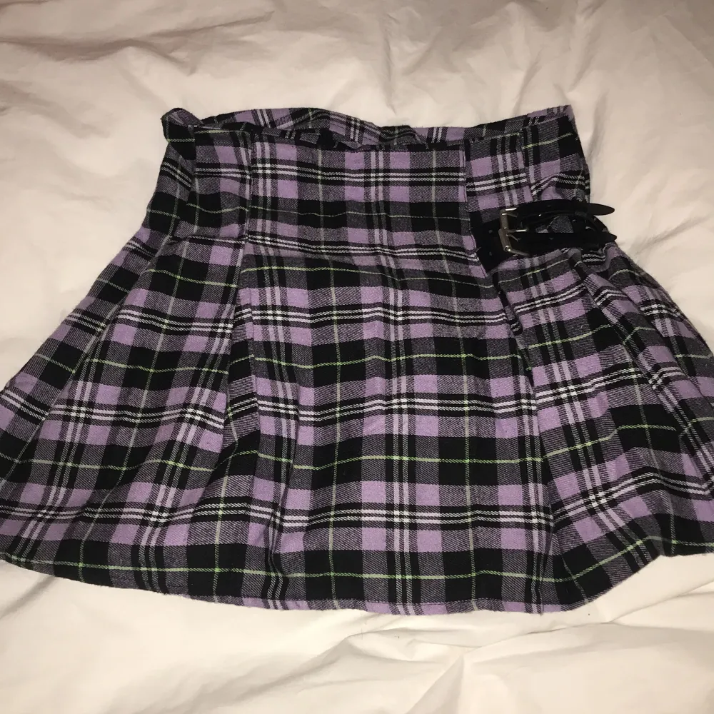 En kort kjol som är lila och svart med en liten ”bälte” detalj. Som ny. Sitter fint. Märke okänt tyvärr. Kjolar.