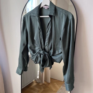 Grön blus - Använd men i gott skick. Satin-skjorta från Victoria’s Secret med knyte framtill. Kan även knytas baktill. 