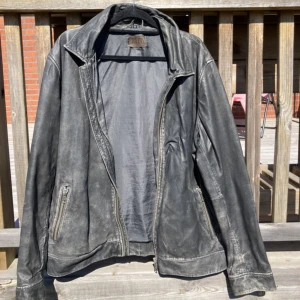 Svart Skinnjacka  - Snygg svart skinnjacka från JOFAMA. Jackan är lite sliten på områden som kanten av kragen, ärmar och sömmarna vilket har lätt till att färgen försvunnit till viss del. Fickor på både insidan och utsidan. Insidan är fin och ren. Originella pris runt 2000:-