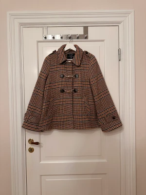 Rutig jacka  - Mönstrad jacka från Atmosphere i storlek UK 10. Skulle säga att det är en 36/38. Strukturvävd. Knäpps med tre knäppen ”haspar” fram på. Fickor. Detaljer med knappar på armarna, axlarna och ryggen. Lite ”klockad”. Läs fortsättning i kommentarerna!!!!!!!!!!