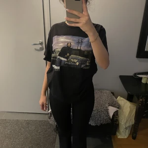 T-shirt med tryck  - En svart T-shirt med tryck på. Den är i storlek L och är i 100% bomull.   Mått: Axelbredd: 48 cm Längd: 76 cm 