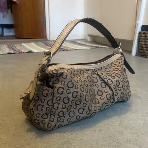 Y2k väska - Säljer denna söta y2k väska. Lite skavanker då den är använd. Vet ej märke. Troligtvis ripoff på guess. I baguette modell.