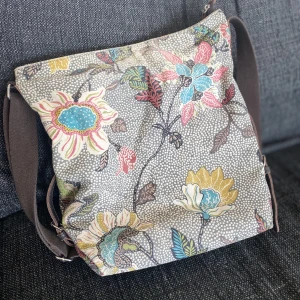 Ceannis shoulder bag   - Ceannis Shoulder Bag är en klassisk axelremsväska i linne och bomull med lädertrimming. Väskan är väldigt lätt. Det rymliga facket ger plats åt A4-format. Reglerbar axelrem i canvas samt reglerbara spännen på sidorna. Brun bas. Storlek: B34*H35*D11CM