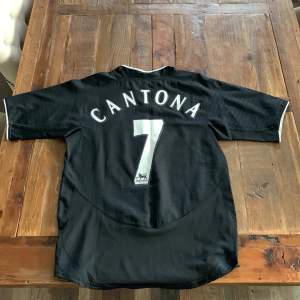 Uniteds jättesnygga bortatröja från 03/04 med Cantona på ryggen. 9/10 skick. Äkta. Cantona la av med fotboll 1997 men vann ”player of the decade” 2003 och då sålde United deras dåvarande tröja med Cantona som hyllning. Skriv för fler bilder eller frågor!