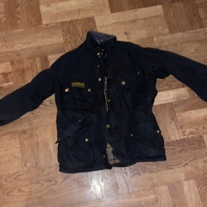 Barbour International Jacka  - Vaxad motorcykeljacka från Barbour International, tillverkad i en kraftig 8oz Sylkoil vaxad bomullsväv. Barbours klassiska, ikoniska motorcykeljacka som tillverkats sedan 1936.  Har använts en säsong vid fåtal tillfällen. 