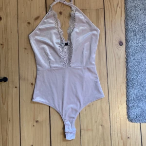 Body med spetsdetaljer - Säljer denna väldigt fina bodyn som knyts i nacken med spetsdetalj i fram. Sparsamt använd och i väldigt fint skick.