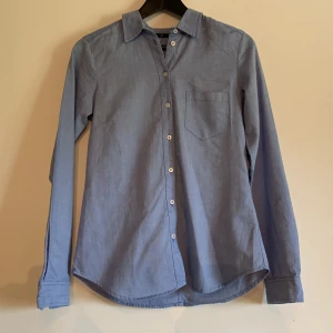 Blå skjorts - Blå skjorta från Åhléns. Använd en del men inget synligt slitage. Storlek 34, men rätt stor i storlek så skulle säga mer åt 36-hållet. 