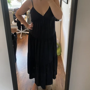 Svart långklänning - Svart långklänning med volang och knytning i ryggen från Bikbok storlek L. 100kr plus frakt