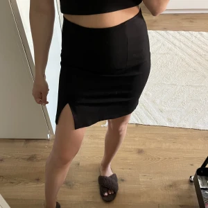 SVART KJOL M SLITS - Svart kjol med en liten slits i sidan vid ena benet