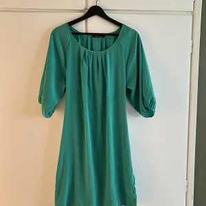 Grön Midi-klänning, nyskick - Grön midiklänning med knytband i midjan. Ballongen och rynkning vid halsringen. Storlek S Endast använd en gång, utan synliga tecken på användning. Obs! Färgen är mycket med klargröna i verkligheten 