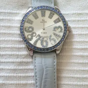 Guess klocka i rostfritt stål med ljusblå strass. Ljusblått krokodilpräglat armband.