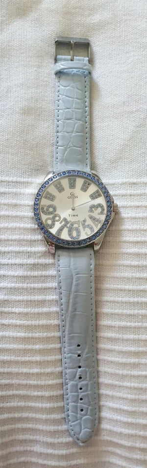 Guess klocka - Guess klocka i rostfritt stål med ljusblå strass. Ljusblått krokodilpräglat armband.