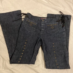Bootcut jeans med detaljer - Coola bootcut jeans med Thirteen vibes. Jeansen har snörning vid midjan, små hål på framsidan, dragkedjor som bakfickor och rhinestones på 1 bakficka! Inga skador eller fläckar! Passar xs/s med en innerbenslängd på ca 80cm