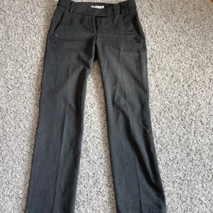 Lågmidjade kostymbyxor - Grå kostymbyxor som sitter väldigt fint! I relativt bra skick(saknas knap på bakfickan men inga andra defekter). Säljer då de är något för små på mig som brukar ha storlek 36/S i byxor💗Inköpta för 600 kr.