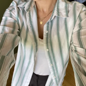 Skjorta - Randig skjorta från bikbok, använd nån gång sådä. Färgen är en blandning mellan grå blå och grön, passar fint över ett vitt linne förslagsvis. 