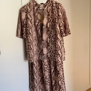 Set med kjol och topp  - Ett supersnyggt set med kjol och kortärmad kjorta från Gina Tricot. Beige/rosa och brunt mönster. Har tyvärr blivit för litet för mig.. fin till allt som sommaren har att erbjuda! 