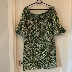 Klänning  - Kort snygg grönmönstrad klänning från H&M. Singoalla-ringning och halvlånga klockade armar. Sparsamt använd. 97% bomull, 3% elastan.