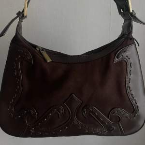 Brun handväska/baguetteväska med snygga detaljer i ”mocka” och ”läder”, relativt rymlig. Köpt second hand men aldrig använd! (Se sista bild för defekt)