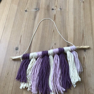 Prydnad  - Detta är en prydnad i garn som jag gjort själv. Den kan även hängas upp. Färgerna är vit rosa och lila. Jag har haft den på mitt rum länge men vill bli av med den nu.🧶🩵