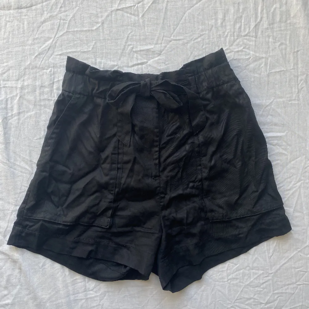 Shorts i tyg med knytdetalj på framsidan och långa fickor. Blixtlås och knapp. . Shorts.