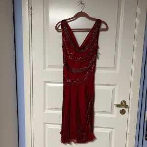 Oanvänd Festklänning - Festklänning likt 1920-tals stil med pärlor & paljetter. Står storlek L på den, men är en större stl 38. Pärlorna gör klänningen tyngre så att den hänger över kroppens form. Färgen tydligast på bild 3. Få pärlor av längs sömmarna men finns extra.