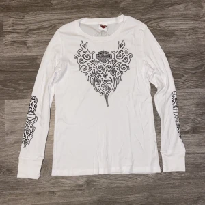 Harley Davidsson långärmad  - En vit Harley Davidsson långärmad tröja (dam). Storlek L. Mått: Längd ca 67cm. Armhåla till armhåla ca 45.5cm