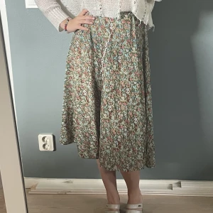 Blommig kjol vintage  - Grön kjol med röda och blåa blommor.  Sitter högt i midjan och är gjort av ett tunt material.  Få tecken på användning 