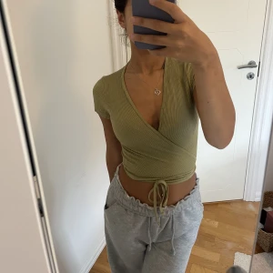 Olivgrön omlott topp - En olivgrön omlott topp med justerbar knut i storlek S, köpt från urban outfitters! Materialet är otroligt mjukt och skönt. Eftersom att den är i stretch så kan den även passa någon i XS så som en i M. Tyvärr kom inte toppen i användning för mig😊