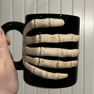 mugg med skelett hand - en jättefin mugg med en skelett hand 🦴vet ej om den går att ha i ugnen/mikron/diskmaskinen, så jag skulle låta bli att göra det. diametern är ungefär 8,5 cm, och den är köpt på flying tiger :)