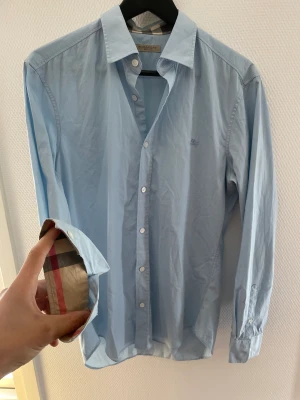 Burberry skjorta ljusblå - Fin burberry skjorta i bra skick. Inga fläckar eller defekter, nyare årsmodell. Självklart äkta, sitter tts/passar lite större