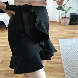 Svart volangkjol i storlek 36 - Svart omlottkjol med dragkedja i ryggen från Boohoo i storlek 36. För liten för mig tyvärr, knappt använd och i superfint skick!