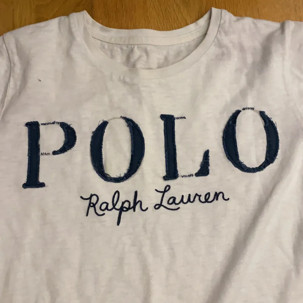 En vit Polo Ralph Lauren T-shirt. Använd ett part gånger för ca 3/4 år. Vit/beige aktig färg med blå text.. T-shirts.