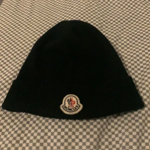 Moncler Mössa - Skick 9.5/10. Superbilligt. 100% äkta. Topp kvalité. Nypris 1899kr. QR-koden är lite skadad pga tvätt men etikett medföljer såklart.