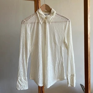 Genomskinlig stretchig skjorta - Vit skjorta med struktur i stretchigt material, figursydd. Strl M