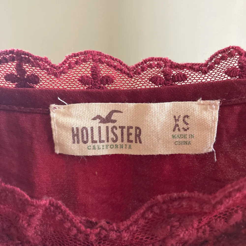 Vinrött linne från Hollister med spets på toppen. Köptes för flera år sedan men har inte använts många gånger. Axelbanden är reglerbara.. Toppar.