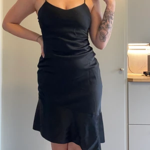 Svart sidenklänning med sne volang  - Klänning från H&M. Strl S. Väldigt bra skick, endast använd 1 gång. Ungefär knälängd på mig som är 172cm. Kroppsnära passform. 