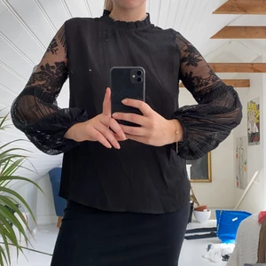 Svart långärmad blus med spetsarmar - Plagget är i jättebra skick, har aldrig använts. Armarna är i blommigt nät och ballongformade i nedre delen av armen. Blusen är i storlek S. 