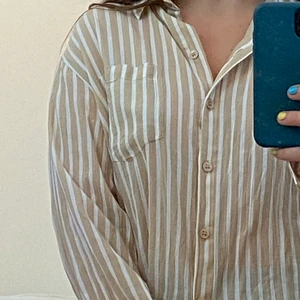 Beige randig skjorta - Säljer denna jättesköna skjorta från monki, perfekt att slänga över en tröja eller till stranden!