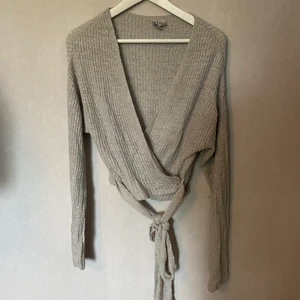 Stickad omlott - Ljusgrå tunn stickad omlott tröja. Bandet längs ner knyter man runt midjan. Du står för frakten.