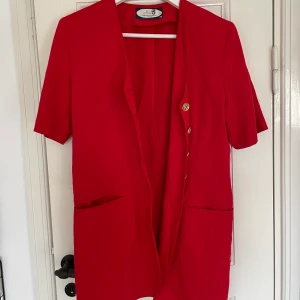 Lång kavaj  - Snygg röd kavaj med guldknappar och axelvaddar. Nästan aldrig använd så väldigt bra skick. Spårbar frakt med DHL inräknad i priset!!
