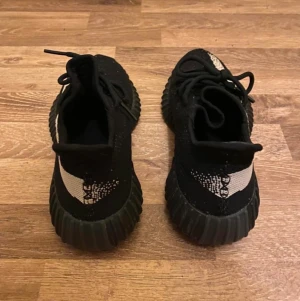 YEEZY 350 V2 OREO - Yeezy Boost 350 V2 'Oreo' släpptes den 17 december 2016 och har en svart Primeknit-överdel med en vit rand, SPLY 350-märke och en genomskinlig svart mellansula i full längd Boost.   Aldrig någonsin använda utan ligger fortfarande i kartongen sen slutet av 2016. Storlek 41 och en tredjedel. Unisex modell 