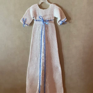 Virkad dopklänning  - Vit virkad dopklänning, vackert mönstrad fram, öppen bak gör den lätt att ta på. Helt ny aldrig använd. Passar från 0-9 månader. Kan levereras med blått eller rosa sidenband. Frakt tillkommer. 