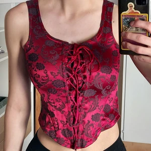 Röd korsett  - Korsettopp med en dragkedja på ryggen och som går att justera med snöret. Passar S och förmodligen en M med 