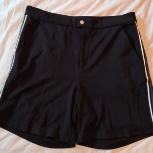 Svarta Björn Borg-shorts - Svarta shorts från Björn Borg med vit/svart/blåa ränder på båda sidor. Björn Borg-tryck på baksidan. 65% viskos, 30% polyester, 5% elastan. Väldigt sköna! Storlek M.
