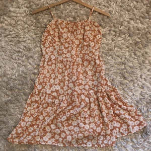 Peach klänning  - Peach/orange färg med vita blommor ,storlek 11-12 yo,säljer den för att den aldrig har kommit till användning(köpare står för frakt)