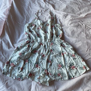 Blomstring jumpsuit  - Säljer denna eftersom jag har vuxit ur den. Den är vit med rosa blommor på och har två fickor på varsin sida. Sömmarna är inte slita eller har gått upp och hela jumpsuiten är i ett bra skick. Den är använd ett få tal gånger. 