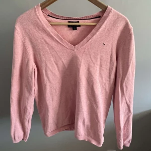 Trendig V-neck tröja - Säljer min rosa Tommy Hillfiger tröja då den inte kommer till användning. Skulle säga att tröjan sitter som en S/M i storleken. Har även en liten blå färgfläck men är inte jätte synlig. 
