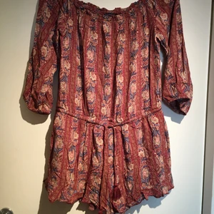 Jumpsuit med korta ben - Vinröd/brun jumpsuit med mönster, från American Eagle Outfitters. Korta ben och trekvarts långa armar. Snörning där fram. Det står storlek L i den, men den passar även mig som vanligtvis har S. Den är i strechigt material. Fått av en kompis men aldrig använt själv. 