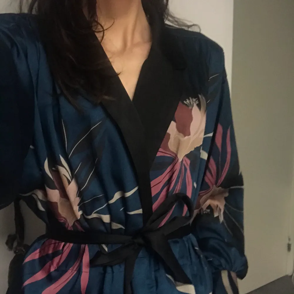 En kavaj/ kimono i silkesmaterial med blommotiv! Antingen kan den knäppas ihop med knapparna, knytas ihop med silkesbandet eller hållas helt öppen. Endast använd fåtal gånger och skicket är därför i princip som nytt. Budgivning i kommentarerna med start på 250 kr.. Kostymer.